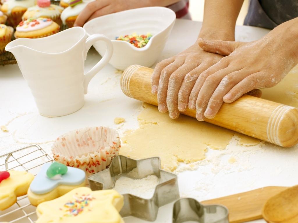 A pair of hands rolling out cookie dough with cookies cutters and cookies